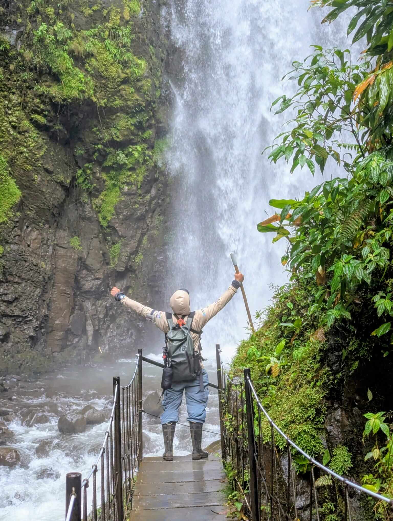 Guía de turismo con los brazos en alto frente a una catarata en el bosque lluvioso de Costa Rica